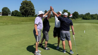 Four men golfers high-five in celebration on the green at the 25th annual Wright County Golf Tournament.