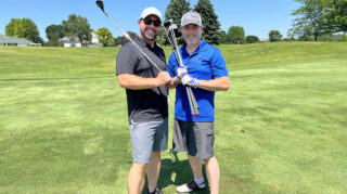 Two men golfers smile while holding clubs on the green at the Community Health Foundation of Wright County Golf Tournament.