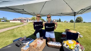 Two ProRehab representatives hold branded golf towels at a sponsor tent with promotional items during the Community Health Foundation of Wright County Golf Tournament.
