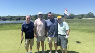 Four golf tournament participants pose on a putting green near a lake during the Community Health Foundation of Wright County Golf Tournament in Buffalo, Minnesota.
