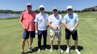 Four golf tournament participants pose with clubs on the fairway beside a lake during the Community Health Foundation of Wright County Golf Tournament in Buffalo, Minnesota.