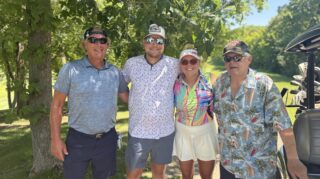 Four golf tournament participants pose near a golf cart under a shaded tree during the Community Health Foundation of Wright County Golf Tournament in Buffalo, Minnesota.