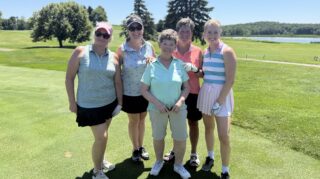 Five golf tournament participants pose on the course with a lake and rolling fairways in the background during the Community Health Foundation of Wright County Golf Tournament.